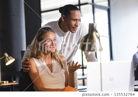 Colleagues collaborating on laptop in modern office, discussing project details 135532764