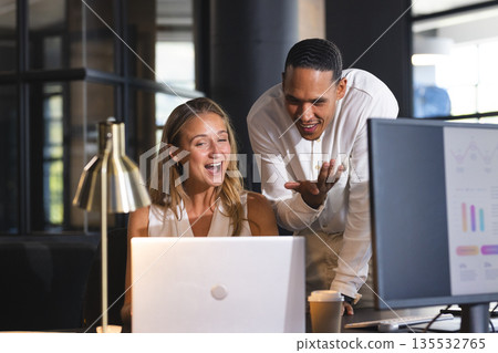 Colleagues collaborating on project, smiling at laptop screen in modern office 135532765
