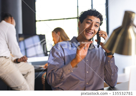 Smiling businessman on phone call in modern office, gesturing while talking Smiling businessman on phone call in modern office, gesturing while talking 135532781