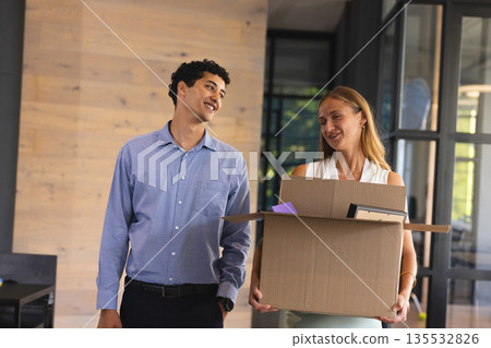 Colleagues smiling while carrying box in modern office, enjoying teamwork Colleagues smiling while carrying box in modern office, enjoying teamwork 135532826
