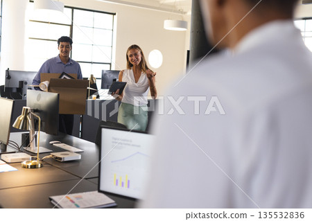 Colleagues welcoming new team member with boxes and tablet in modern office Colleagues welcoming new team member with boxes and tablet in modern office 135532836