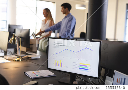 Business professionals discussing data charts on computer screen in modern office 135532840