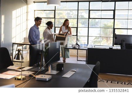 Colleagues in modern office discussing project while holding documents and smiling 135532841