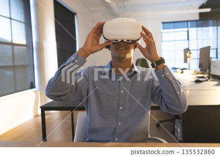 Businessman using VR headset at office desk, exploring virtual reality technology Businessman using VR headset at office desk, exploring virtual reality technology 135532860