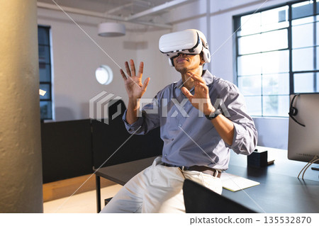 Businessman using VR headset at office, exploring virtual reality with excitement Businessman using VR headset at office, exploring virtual reality with excitement 135532870