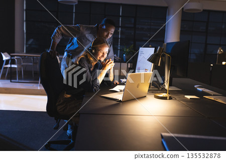 Collaborating on project, colleagues focused on computer screen in office working late Collaborating on project, colleagues focused on computer screen in office working late 135532878