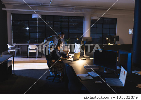 Colleagues working late in office, analyzing data on computer screen together Colleagues working late in office, analyzing data on computer screen together 135532879