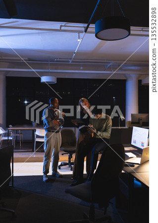 In office at night, business professionals reviewing documents and collaborating together 135532898