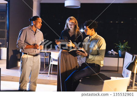 Business team collaborating on digital devices in modern office at night 135532901