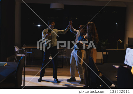 Business professionals celebrating success with high fives in modern office at night Business professionals celebrating success with high fives in modern office at night 135532911