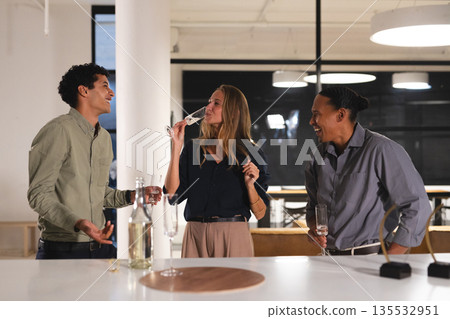 At office gathering, colleagues drinking and laughing, enjoying evening together At office gathering, colleagues drinking and laughing, enjoying evening together 135532951