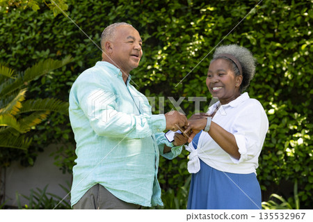 Senior couple dancing joyfully in garden, enjoying sunny day together 135532967
