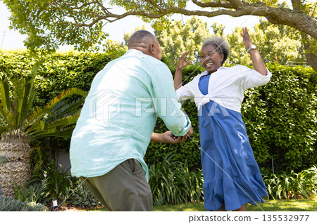 Senior couple dancing joyfully in garden, enjoying sunny day together 135532977