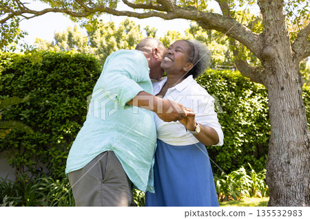 African American senior couple dancing joyfully under tree in sunny garden 135532983