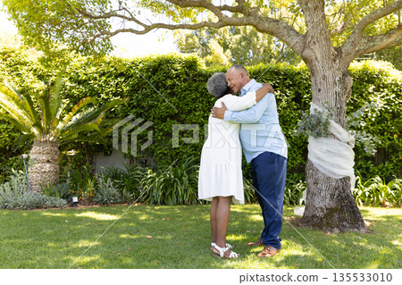 Senior couple embracing under tree in garden, enjoying peaceful outdoor moment 135533010