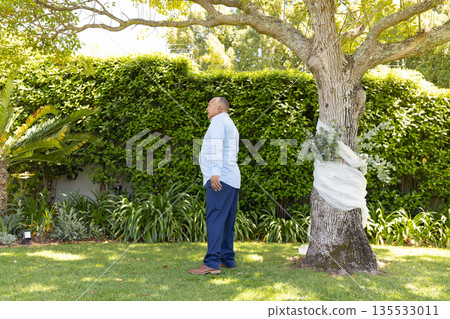 Senior man standing in garden, enjoying peaceful moment under tree Senior man standing in garden, enjoying peaceful moment under tree 135533011