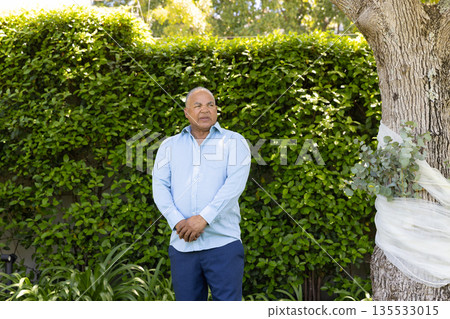 Senior man standing outdoors in garden, looking thoughtful near tree Senior man standing outdoors in garden, looking thoughtful near tree 135533015