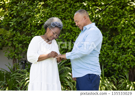 Senior couple exchanging rings in garden, sharing joyful moment together 135533029