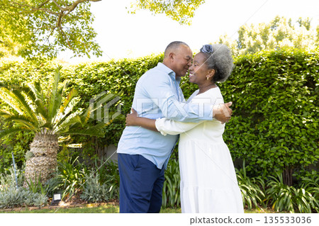Senior couple embracing joyfully in sunny garden surrounded by lush greenery Senior couple embracing joyfully in sunny garden surrounded by lush greenery 135533036