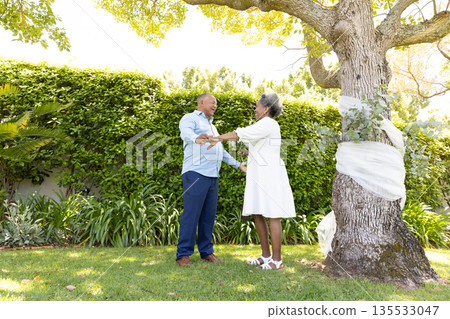 Senior couple holding hands under tree in garden, enjoying sunny day together Senior couple holding hands under tree in garden, enjoying sunny day together 135533047