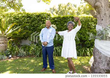 Senior couple enjoying sunny day in garden, woman dancing joyfully beside partner Senior couple enjoying sunny day in garden, woman dancing joyfully beside partner 135533055