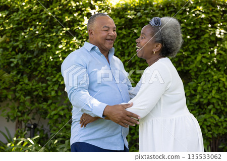Senior couple laughing and embracing outdoors in lush green garden Senior couple laughing and embracing outdoors in lush green garden 135533062
