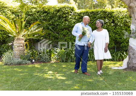 Senior couple walking in garden, holding hands and smiling at each other 135533069