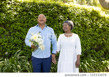 Senior couple holding hands and smiling outdoors with bouquet of flowers Senior couple holding hands and smiling outdoors with bouquet of flowers 135533074