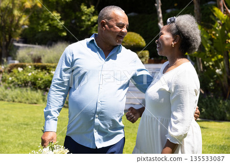 Senior couple walking in garden, smiling and enjoying sunny day together 135533087