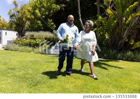 Senior couple walking hand in hand in sunny garden, enjoying outdoor stroll 135533088