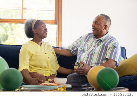 Senior couple sitting on sofa, exchanging gifts and enjoying each other's company 135533123