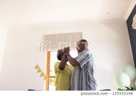 Senior couple dancing joyfully at home, celebrating special moments together 135533146