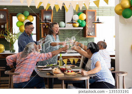 Senior friends celebrating together at home, raising glasses in joyful toast 135533191