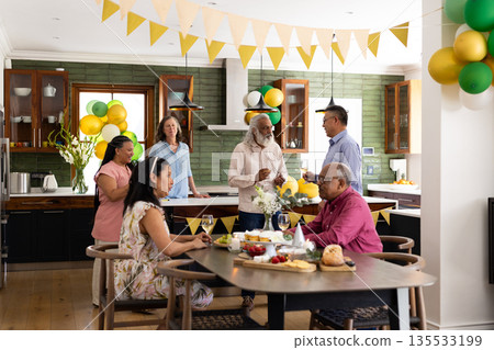 Group of seniors enjoying conversation and drinks at home during festive party 135533199