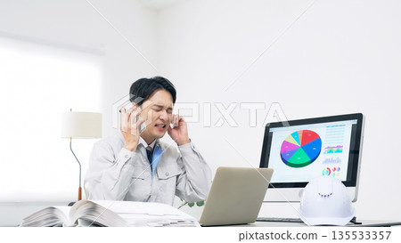 一名男工人一邊用智慧型手機通話一邊憂心忡忡。 135533357