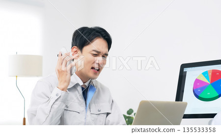 一名男工人一邊用智慧型手機通話一邊憂心忡忡。 135533358