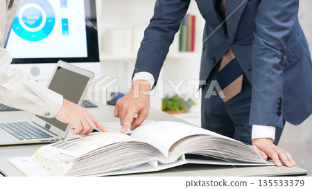A group of business people and workers having a meeting while looking at a catalog A group of business people and workers having a meeting while looking at a catalog 135533379
