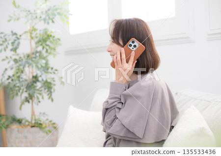 一位老年婦女在房間裡用智慧型手機通話的畫面 135533436
