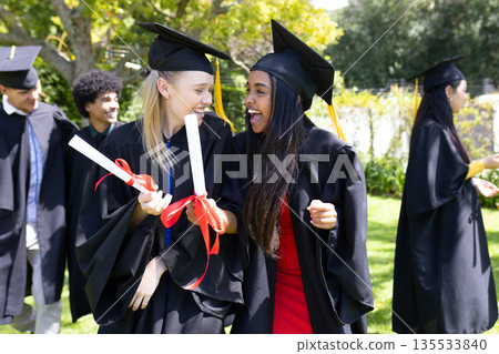 Graduating students outdoors in caps and gowns, holding diplomas and celebrating Graduating students outdoors in caps and gowns, holding diplomas and celebrating 135533840