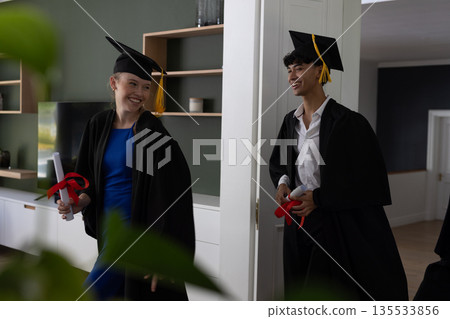 Graduating teens in gowns holding diplomas, celebrating achievement joyfully at home Graduating teens in gowns holding diplomas, celebrating achievement joyfully at home 135533856