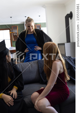 Teen girls celebrating graduation at home, wearing gowns and smiling together Teen girls celebrating graduation at home, wearing gowns and smiling together 135533861