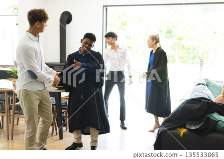 Teen graduates celebrating at home, shaking hands and smiling with friends Teen graduates celebrating at home, shaking hands and smiling with friends 135533865