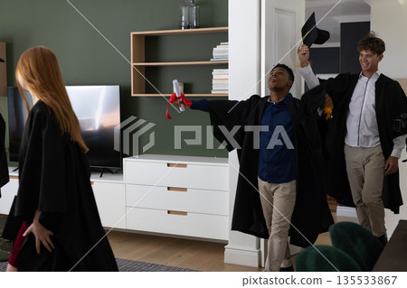 Teens celebrating graduation at home, holding diplomas and wearing caps and gowns 135533867