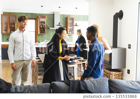 Teens celebrating graduation at home, wearing gowns and chatting happily together 135533868