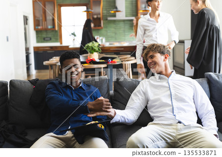 Teen boys celebrating friendship on couch at home, smiling and shaking hands 135533871