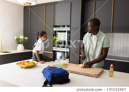 African American father preparing lunch in kitchen with daughter watching happily African American father preparing lunch in kitchen with daughter watching happily 135533887