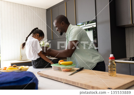 Father helping daughter with school uniform in kitchen, preparing for school 135533889