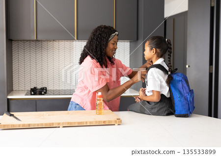 Mother helping daughter with school uniform in kitchen before heading to school 135533899