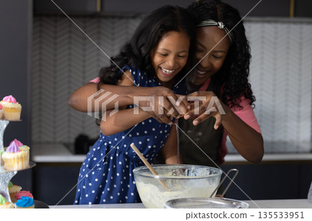 Mother and daughter baking together, cracking eggs and laughing in kitchen Mother and daughter baking together, cracking eggs and laughing in kitchen 135533951