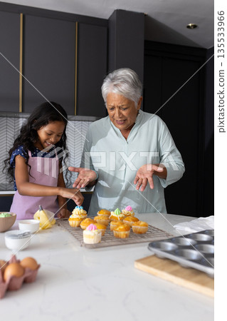 Decorating cupcakes, grandmother and granddaughter sharing laughter in modern kitchen 135533966